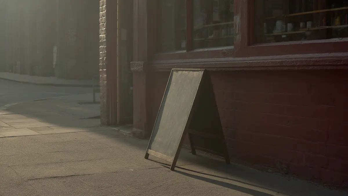 A blank chalkboard sign leaning against a brick shopfront in soft early morning light.