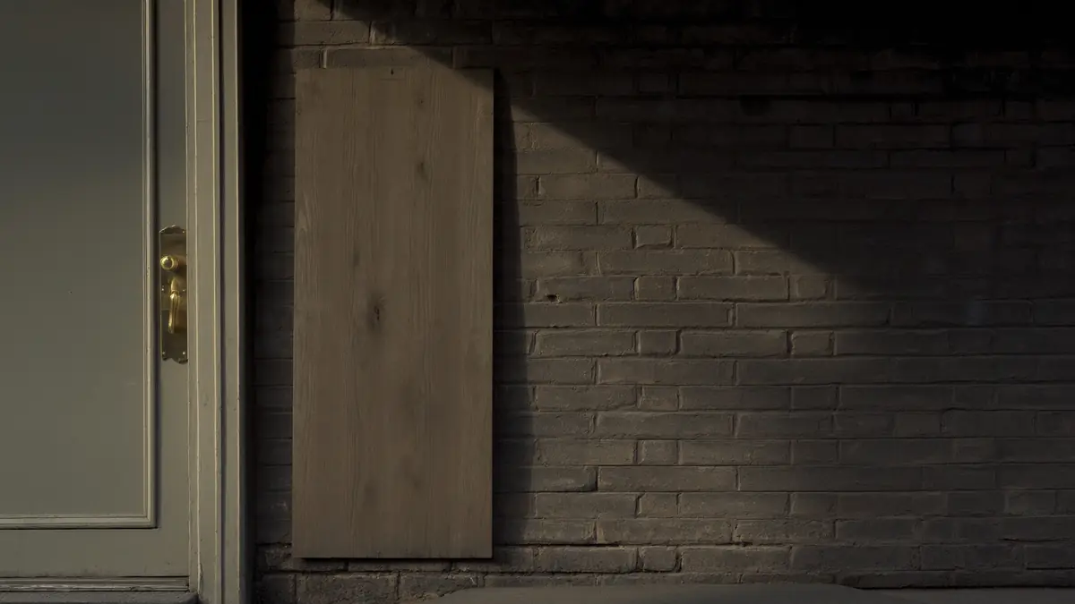 A blank wooden sign board beside a brick shopfront door in soft early morning light.
