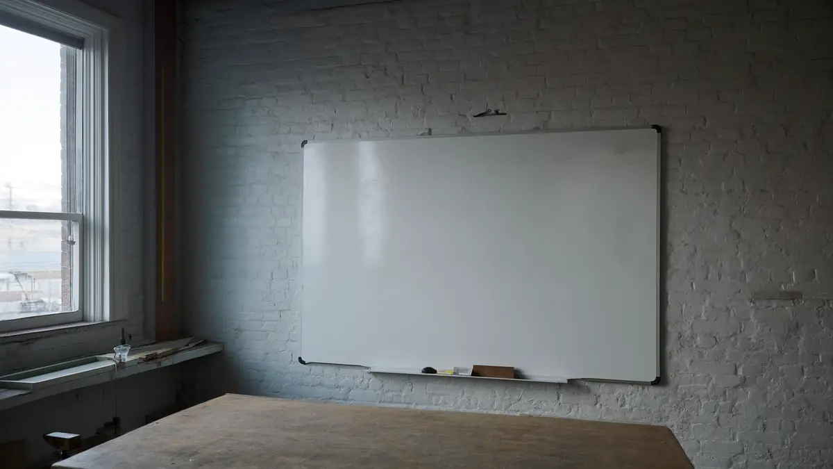 A blank whiteboard on a brick wall in a small workshop, lit by soft morning light from a nearby window.