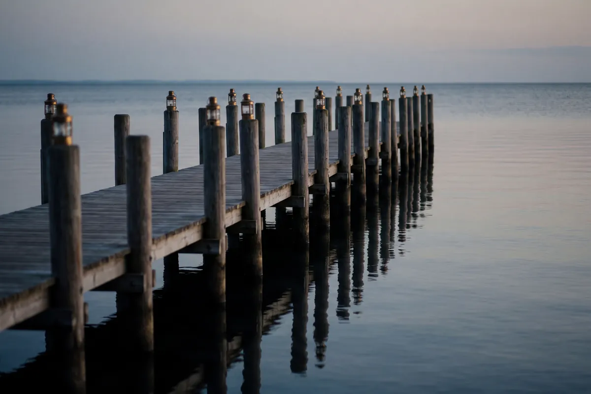An oak jetty running out onto still water at dawn, its mooring posts receding evenly into the mist