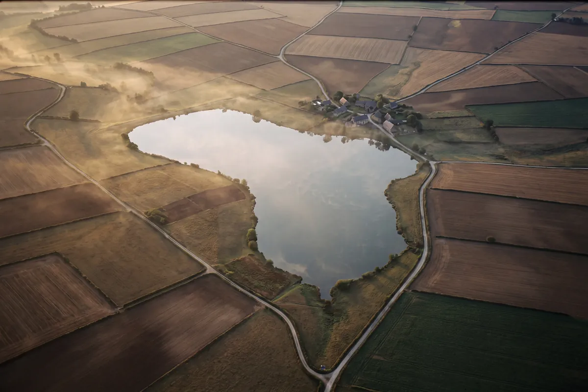An aerial view at golden hour of a lake ringed by fields, with country lanes converging on a village